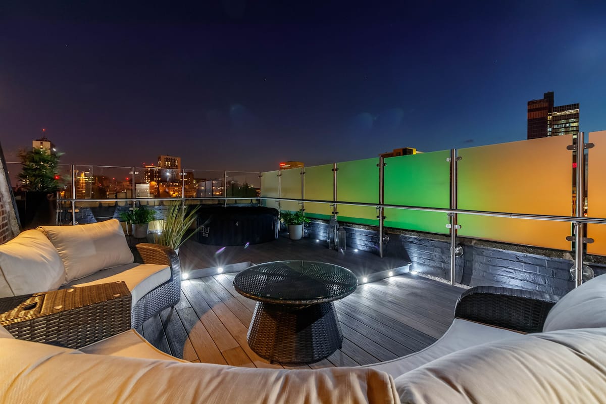 A rooftop terrace with outdoor seating, a glass table, and city views at night.