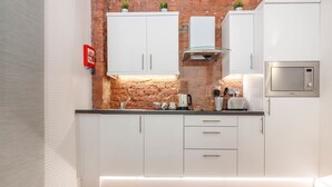 A modern kitchen with white cabinets, a brick accent wall, a stainless steel microwave, and a built-in oven. - Swan Street Penthouse (Manchester)