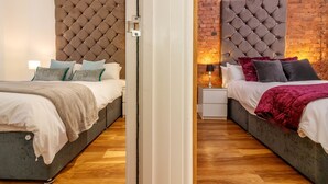 Two adjacent bedrooms with tufted headboards, wooden flooring, and bedside tables with lamps. - Swan Street Penthouse (Manchester)