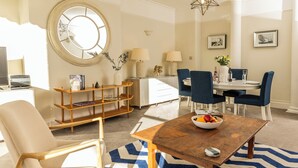 Een moderne woonkamer met een rond raam, een houten bijzettafeltje en een blauw-wit kleed.