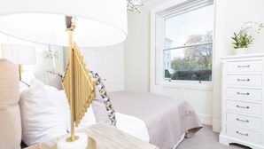 Een keurig opgemaakt slaapkamer met een bed, nachtkastje, lamp, kaptafel en raam.
