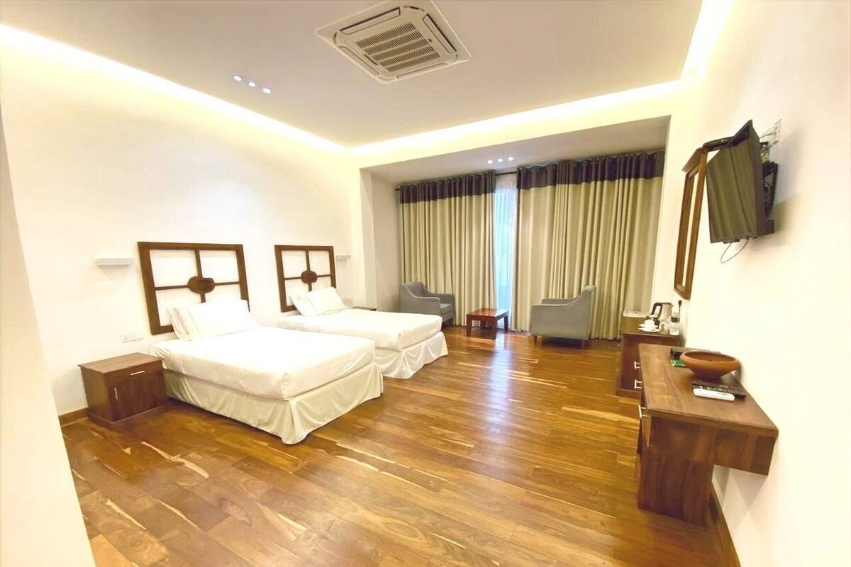 A hotel room with two beds, a desk, a chair, and a large window with curtains.