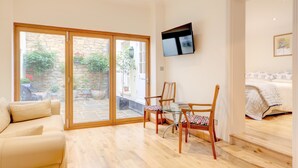A modern living room with a sofa, a dining table with chairs, a TV mounted on the wall, and a staircase leading to a bedroom. - Luxury Apartments - Rodney Road (Cheltenham)