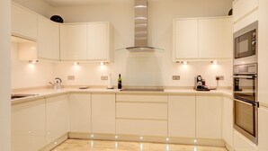 A modern kitchen with white cabinetry, a stainless steel range hood, and built-in appliances. - Luxury Apartments - Rodney Road (Cheltenham)