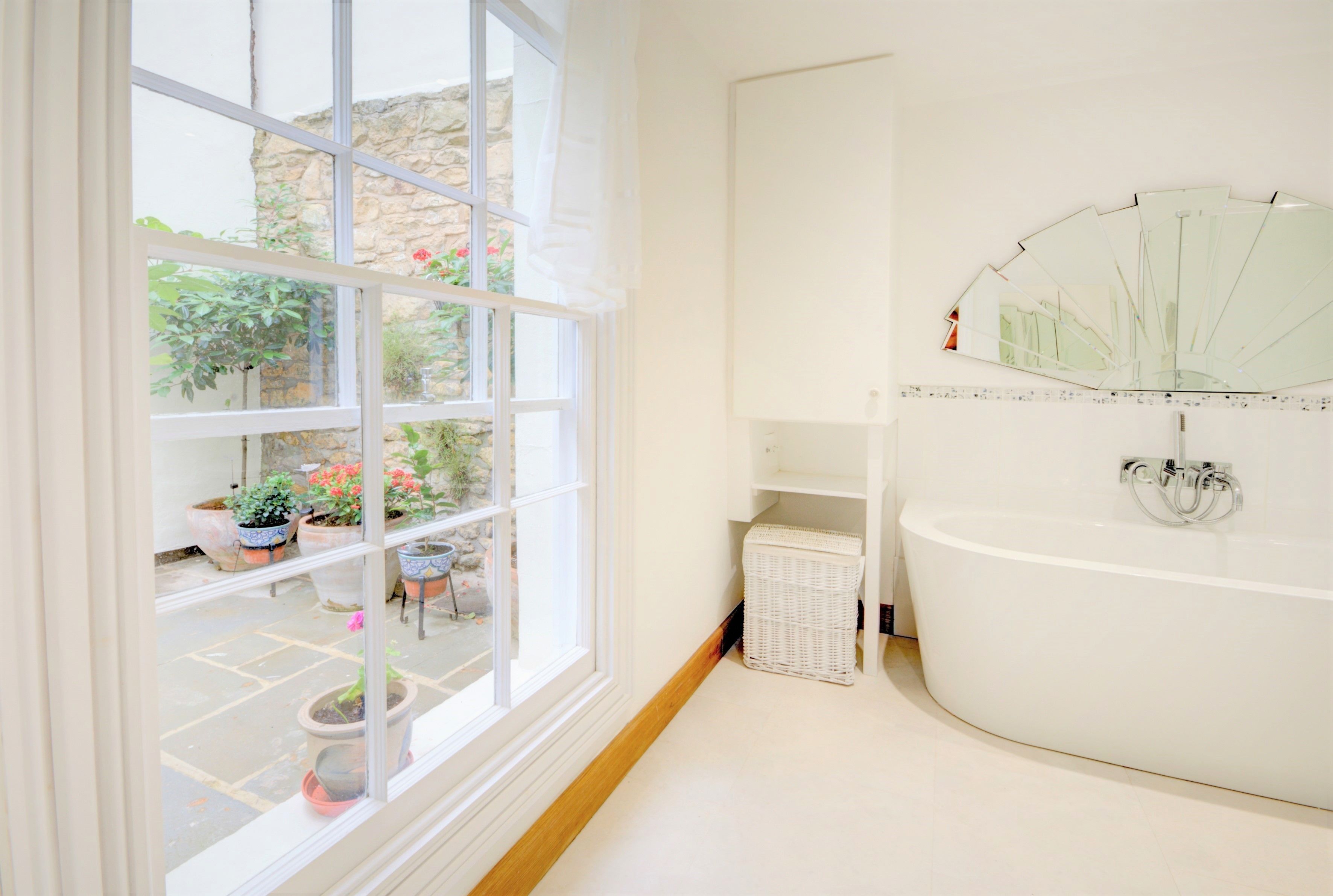 A bathroom with a large window, a bathtub, and a mirror.