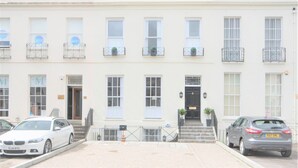 A row of white townhouses with multiple windows, a central entrance, and a small garden area. - Luxury Apartments - Rodney Road (Cheltenham)