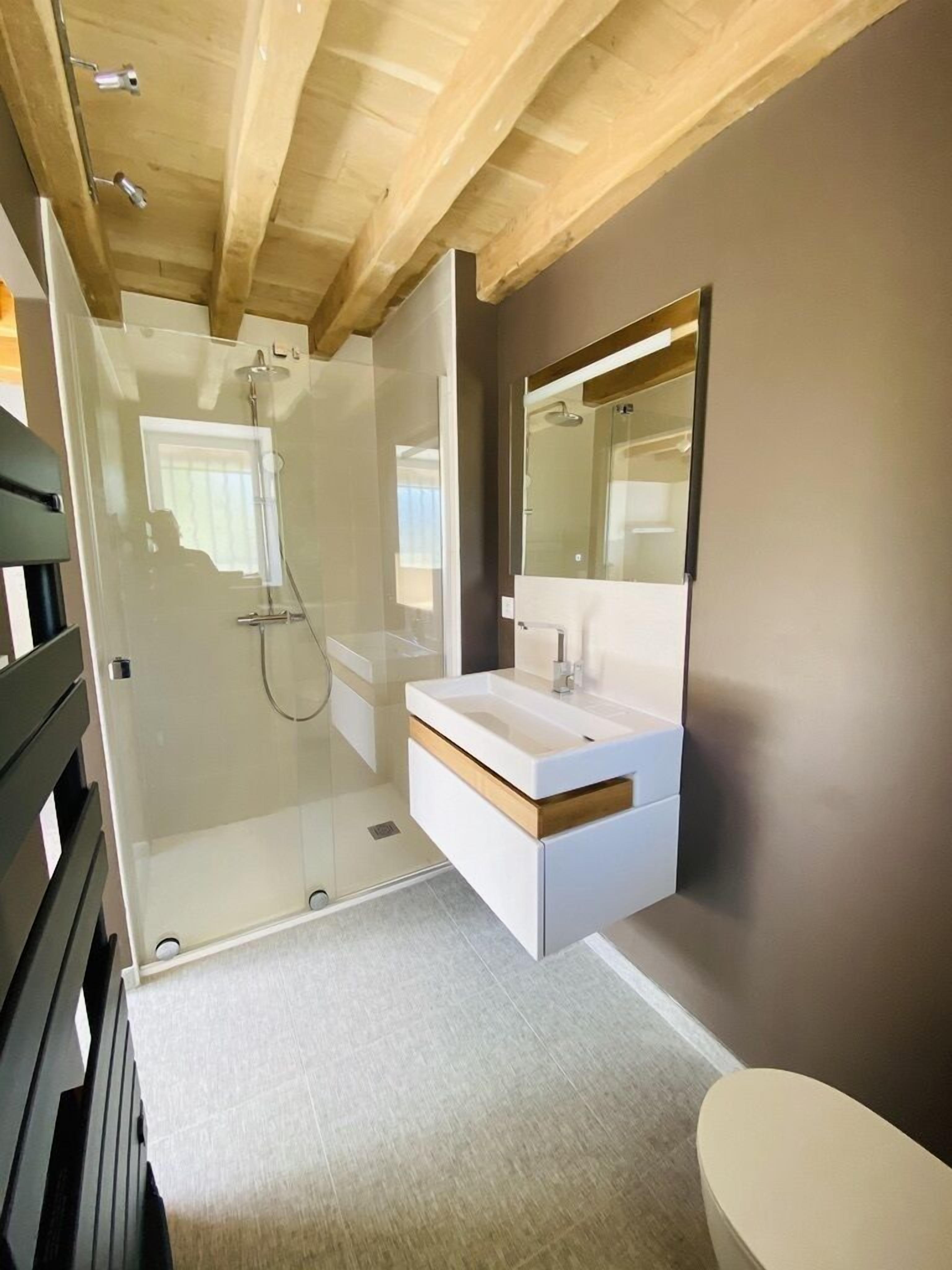 Un baño moderno con cabina de ducha de vidrio, tocador blanco con espejo y techo de madera.