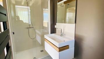 Un baño moderno con cabina de ducha de vidrio, tocador blanco con espejo y techo de madera.