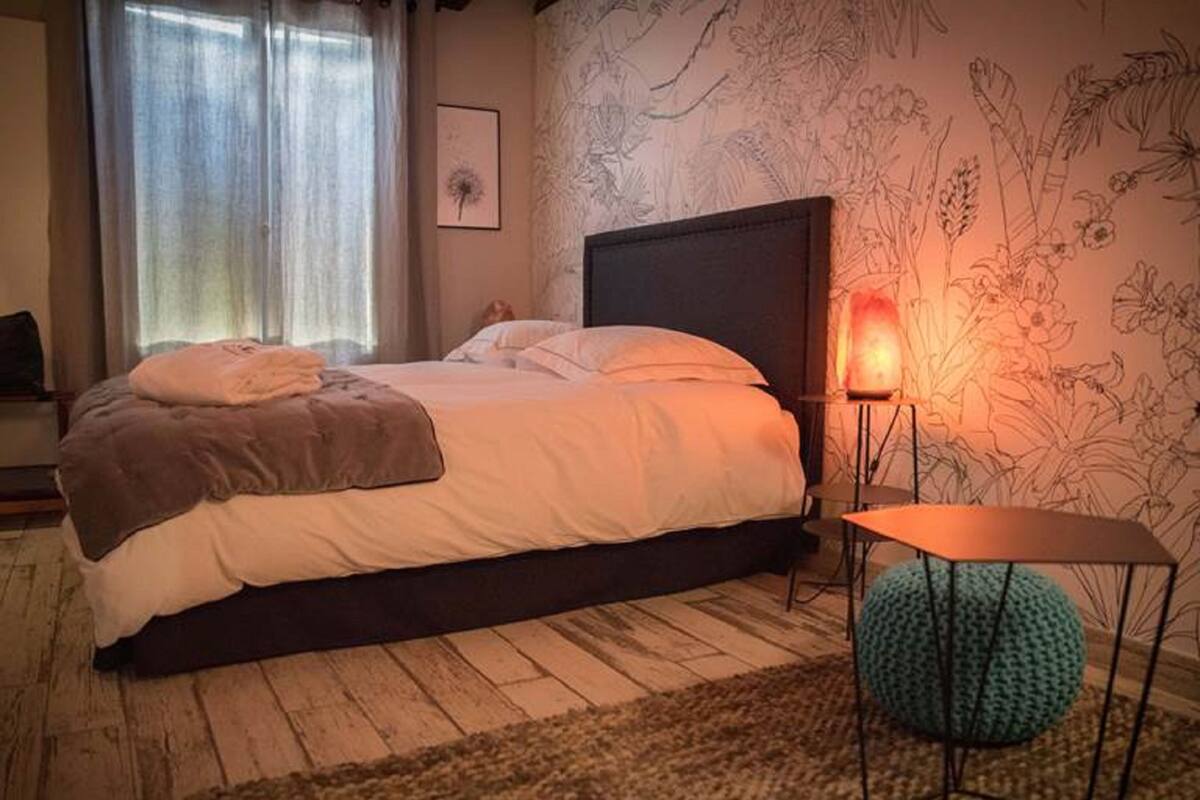 Une chambre à coucher avec un lit, une table de chevet, une lampe et un mur recouvert d’un papier peint à motifs floraux.