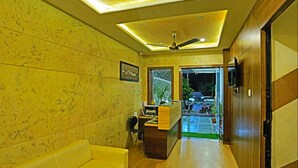 A hotel lobby with a reception desk, a sofa, a ceiling fan, and a view of the outside. - Hotel Suraj Palace (Udaipur)