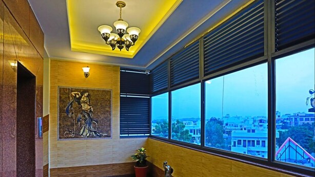A modern hotel lobby with a large window offering a city view, a chandelier, and a decorative bench. - Hotel Suraj Palace (Udaipur)