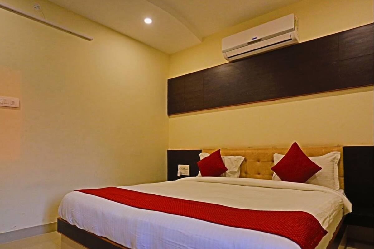Une chambre d’hôtel avec un grand lit, une tête de lit en bois et un appareil de climatisation placé au-dessus.