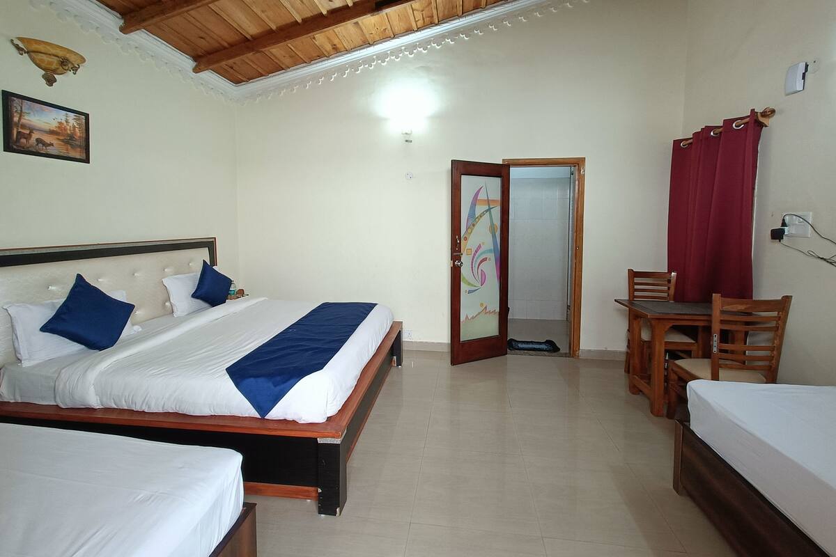 A hotel room with a wooden ceiling, a bed with white bedding and blue accents, a desk with a chair, and a red curtain.