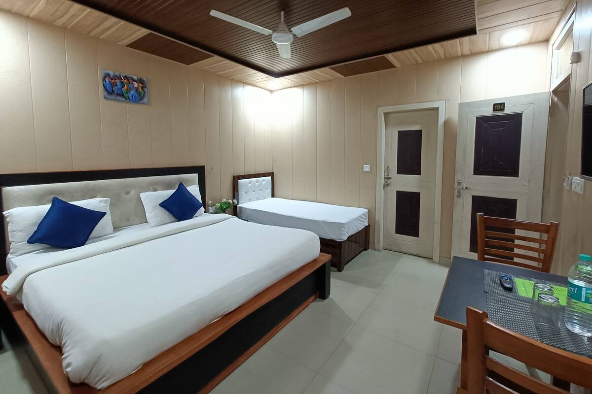 A hotel room with two beds, a ceiling fan, a small table with a chair, and a door with a number.