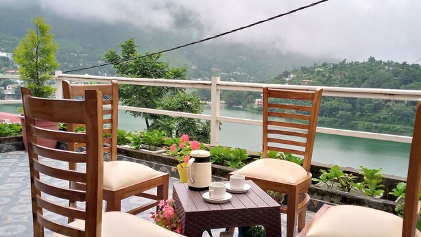 Una terraza con dos sillas de madera, una mesa con tetera, tazas y una planta en maceta.