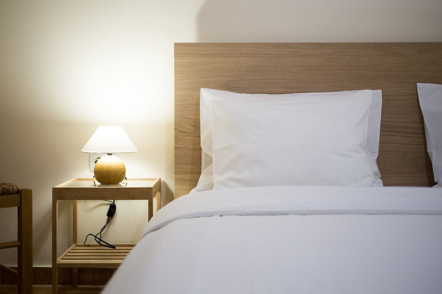 A neatly made bed with white linens, a wooden headboard, and a bedside table with a lamp.