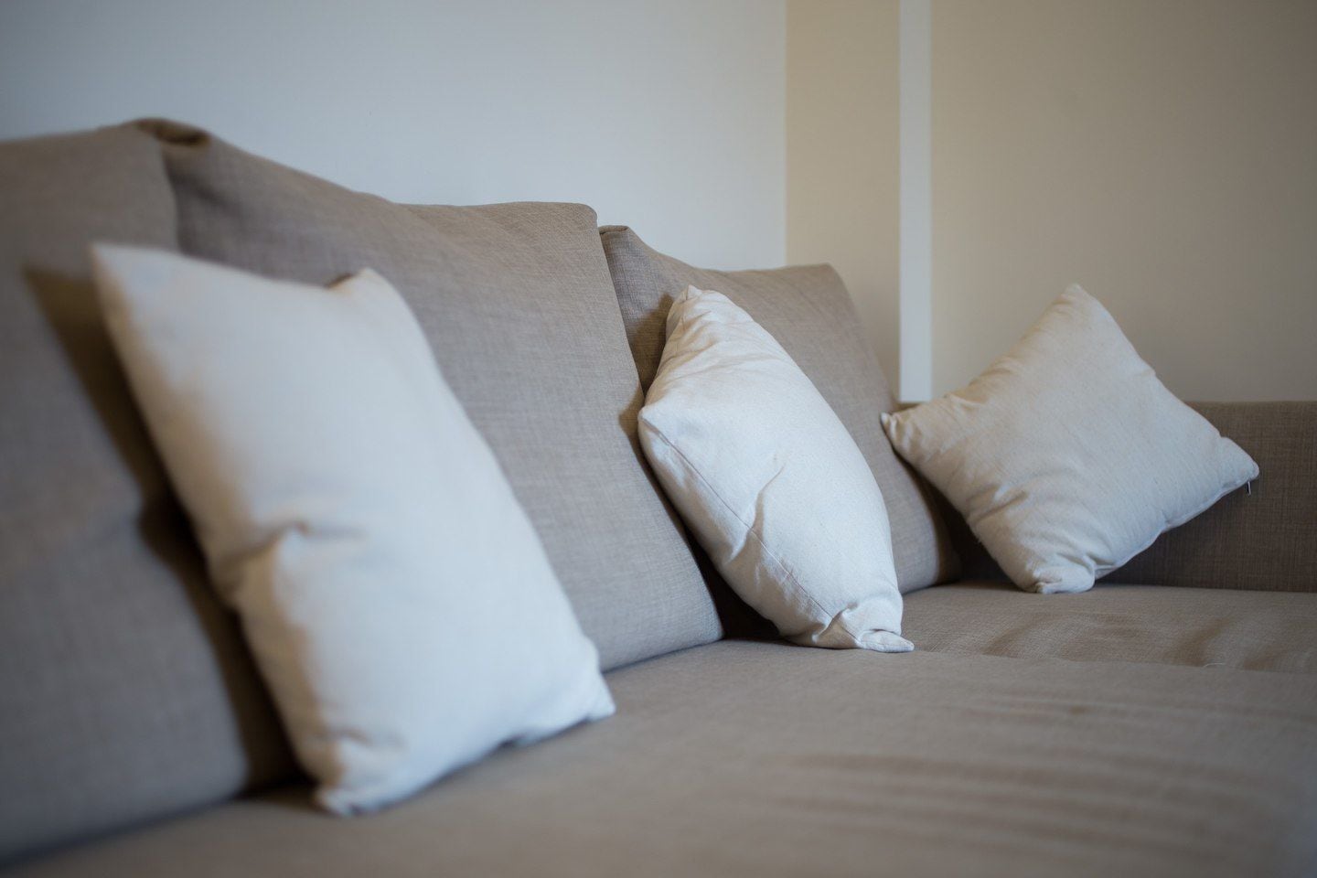 A beige sofa with three white cushions.