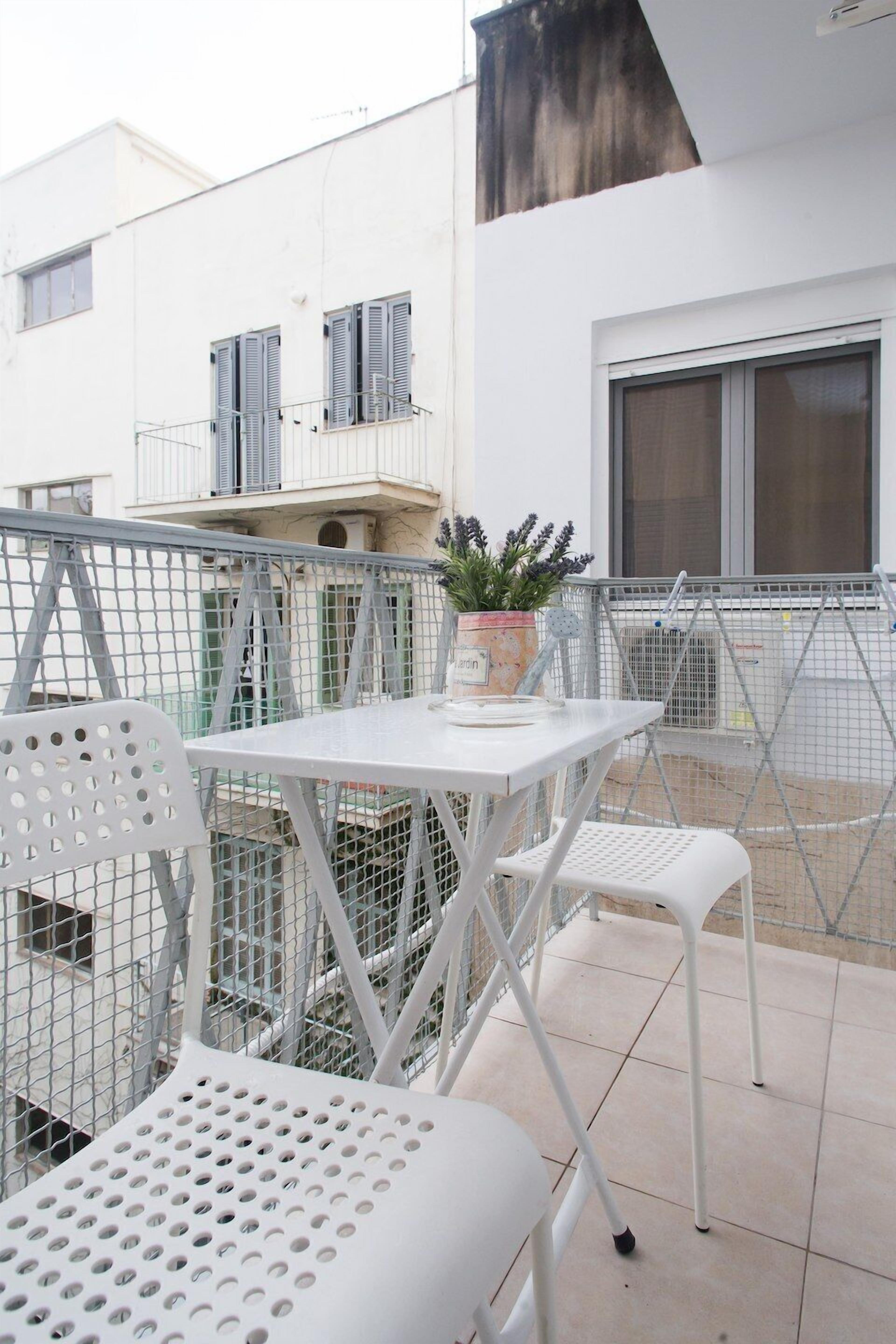 A balcony with a white table and chairs, a potted plant, and a metal fence.