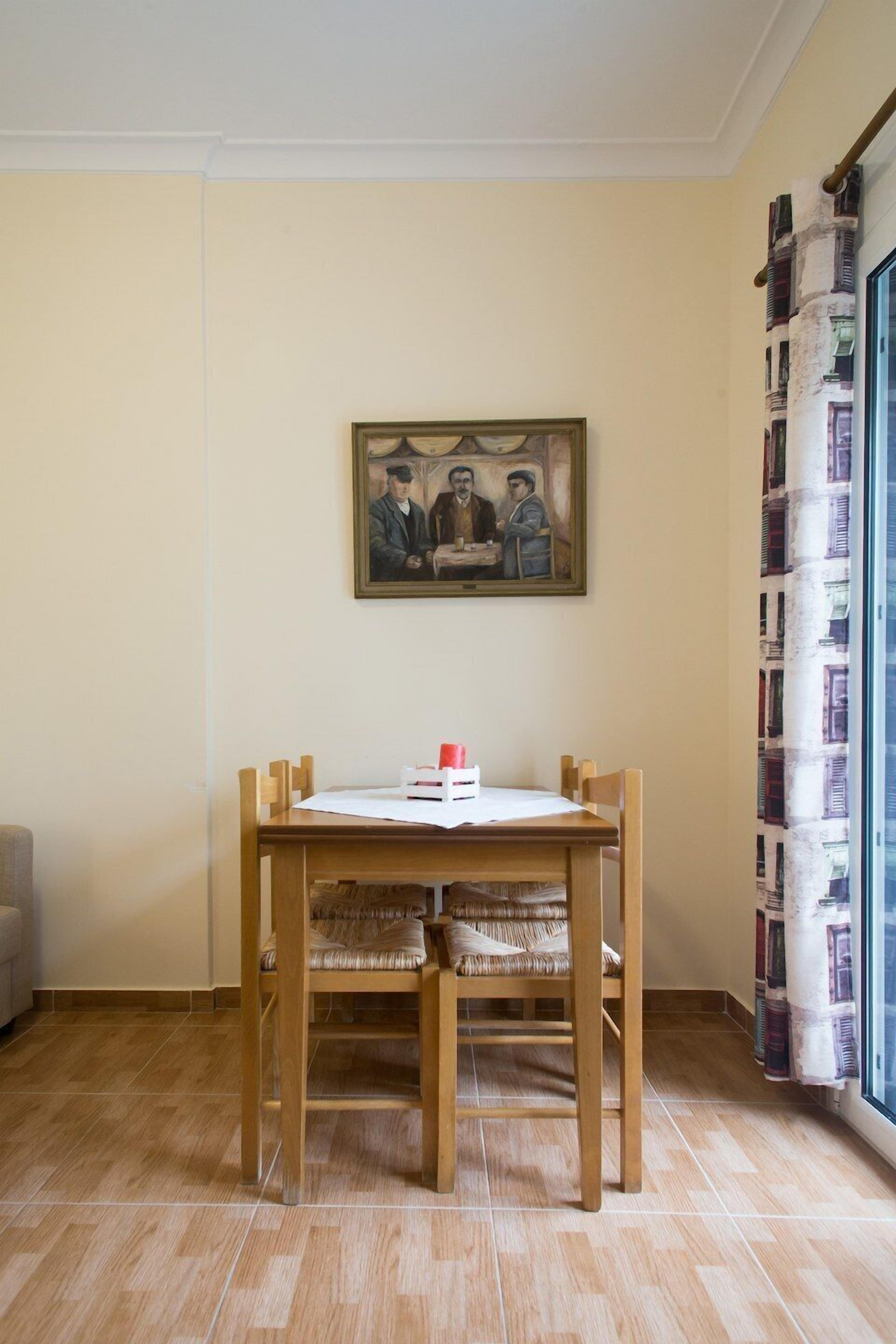 Un comedor con una mesa y sillas de madera, un cuadro enmarcado en la pared y una ventana con cortinas estampadas.