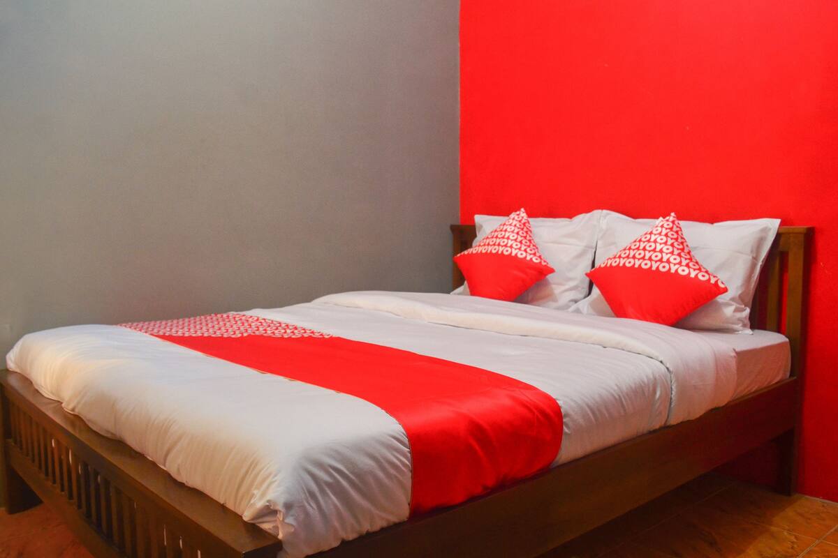 A bed with white and red bedding, a wooden headboard, and a red accent wall.