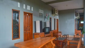 A room with a wooden table, chairs, a television, and a clock on the wall. - OYO 1145 Rita Guesthouse (Pangandaran)