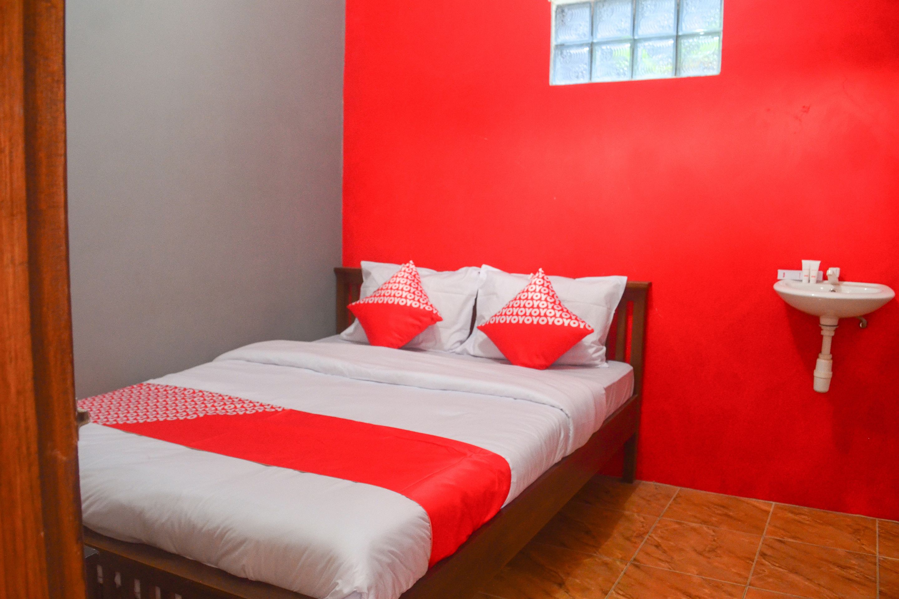 A bedroom with a red wall, a wooden bed frame, white bedding, and a small window.