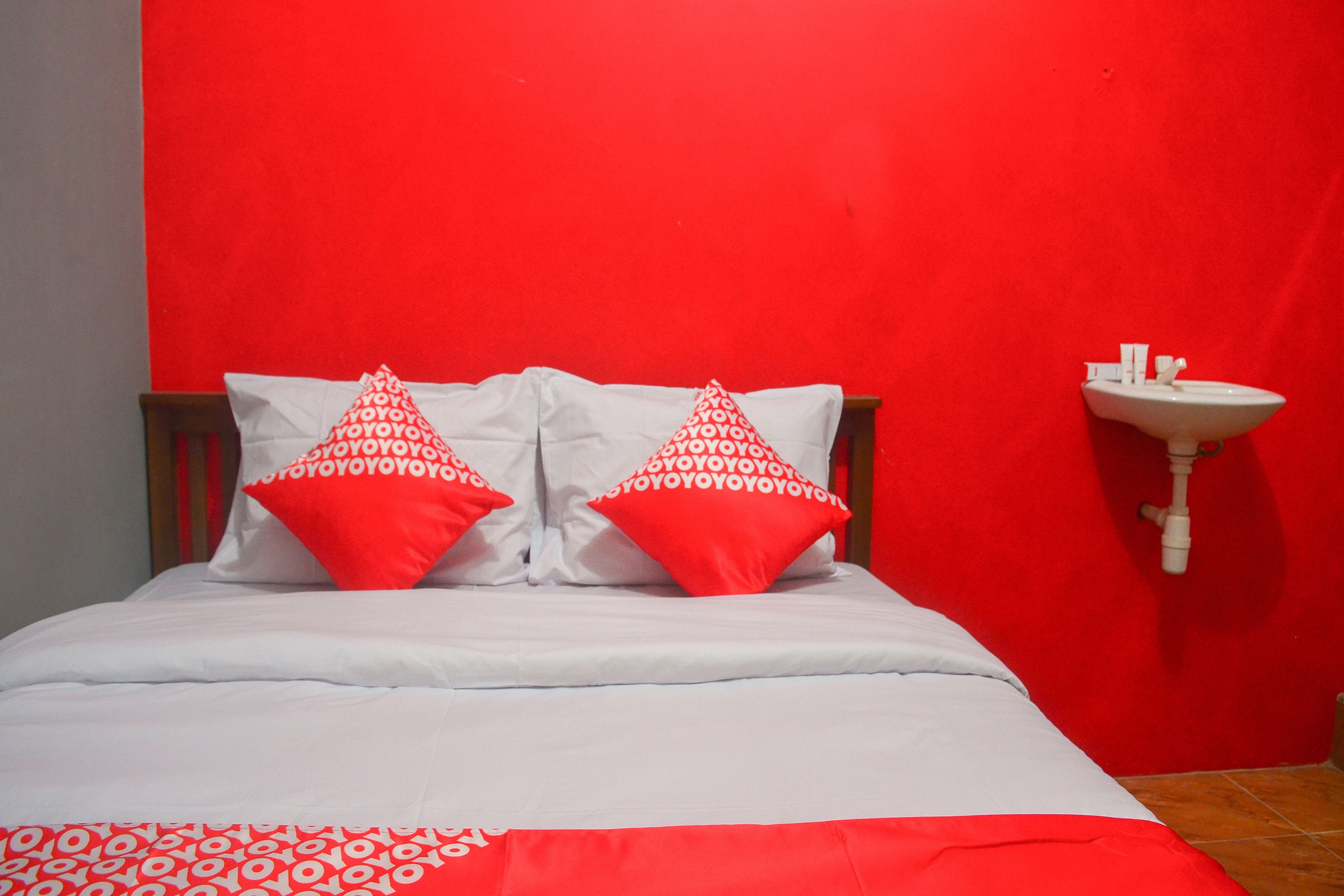 Una cama con ropa de cama blanca y dos almohadas rojas de estampado repetido.