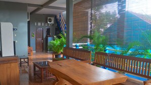 A spacious room with a large wooden table and benches, a small cabinet, and a potted plant. - OYO 1145 Rita Guesthouse (Pangandaran)