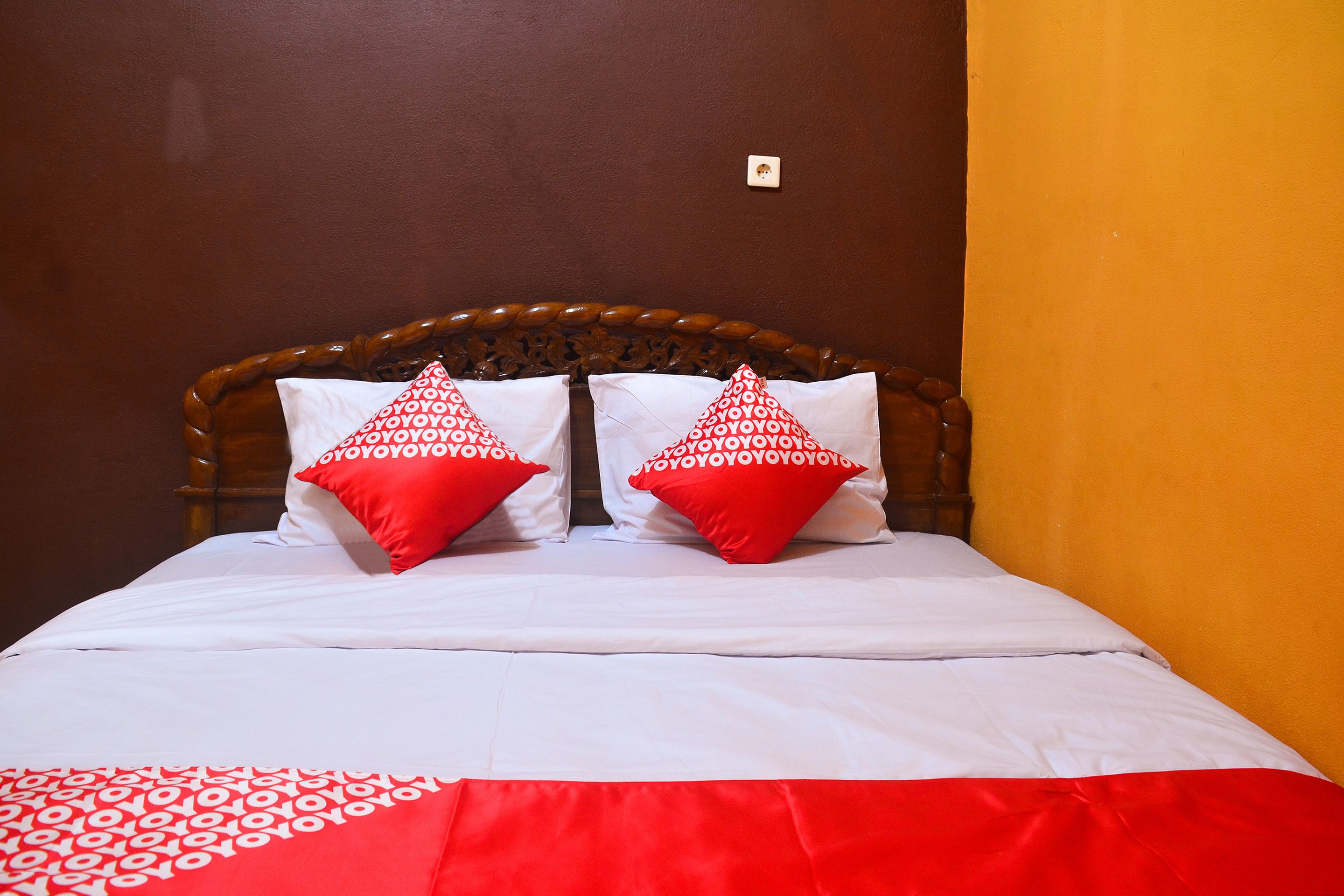 A bed with a wooden headboard, two red pillows, and a white bedspread.