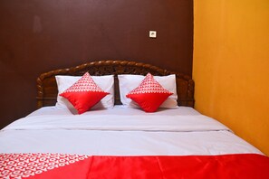 A bed with a wooden headboard, two red pillows, and a white bedspread. - OYO 1145 Rita Guesthouse (Pangandaran)
