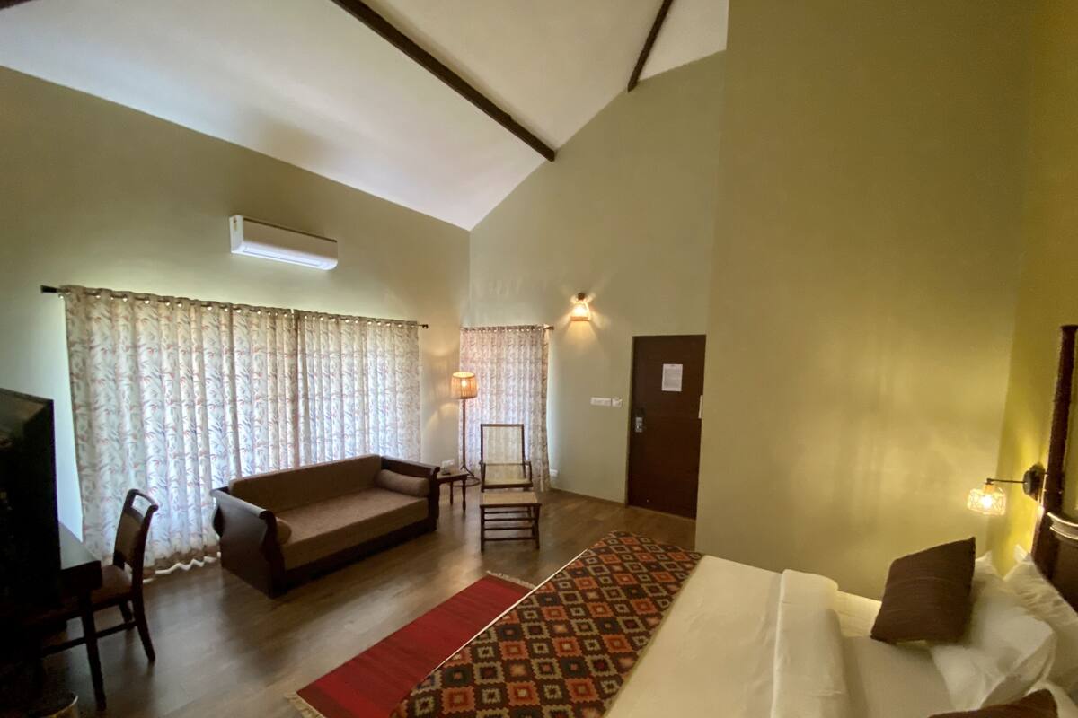 A spacious room with a large bed, a sofa, a chair, and a small table. There is a door and a window with curtains.