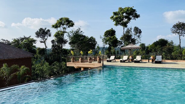 A clear blue pool with lounge chairs and a gazebo, surrounded by trees and a clear sky.