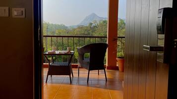 A room with a view of a mountain, a balcony with a table and chairs, and a wooden door.