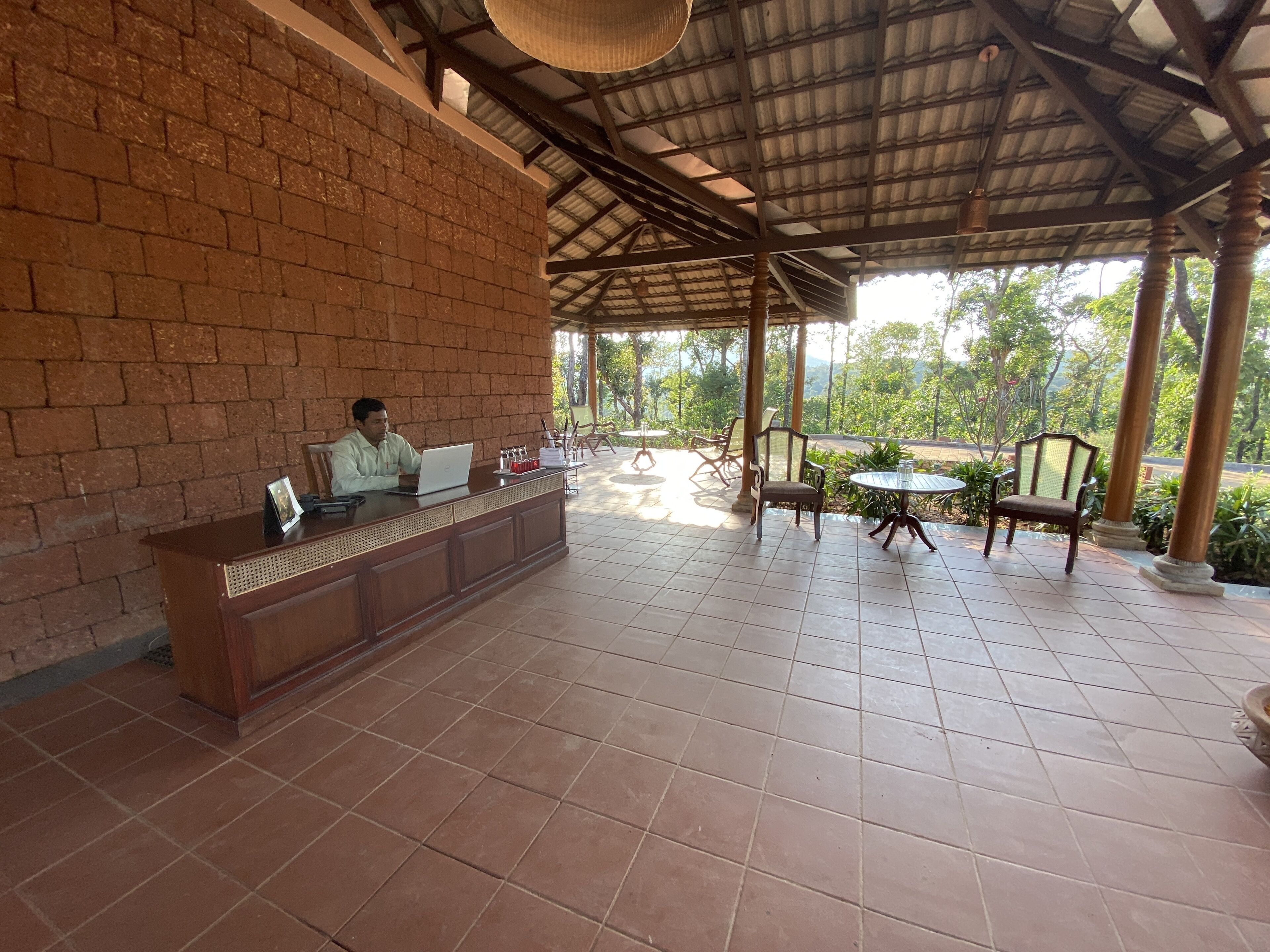 A covered outdoor seating area with a brick wall, a wooden reception desk, and several chairs and tables.