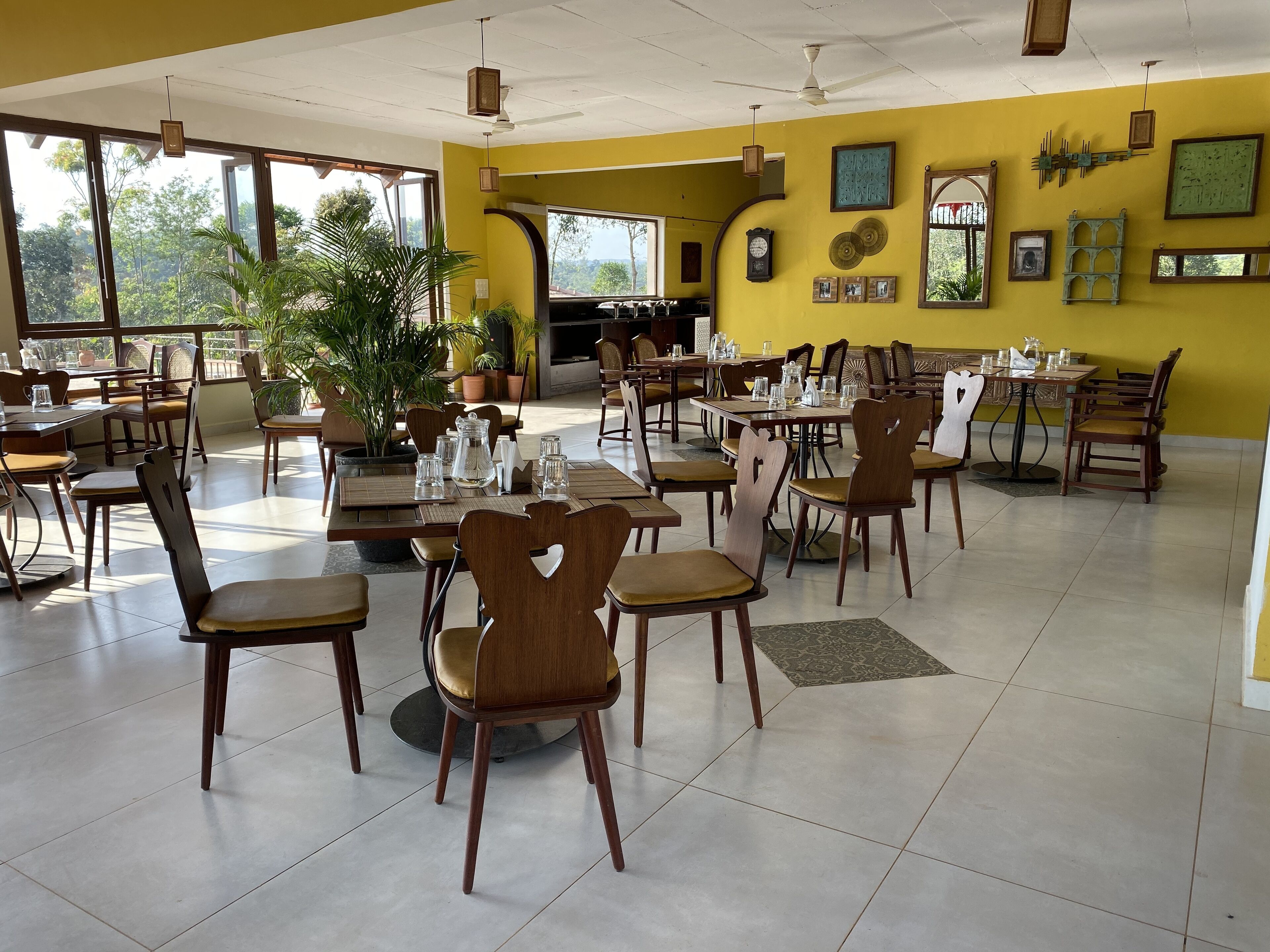 A spacious dining area with multiple tables and chairs, large windows, and potted plants.