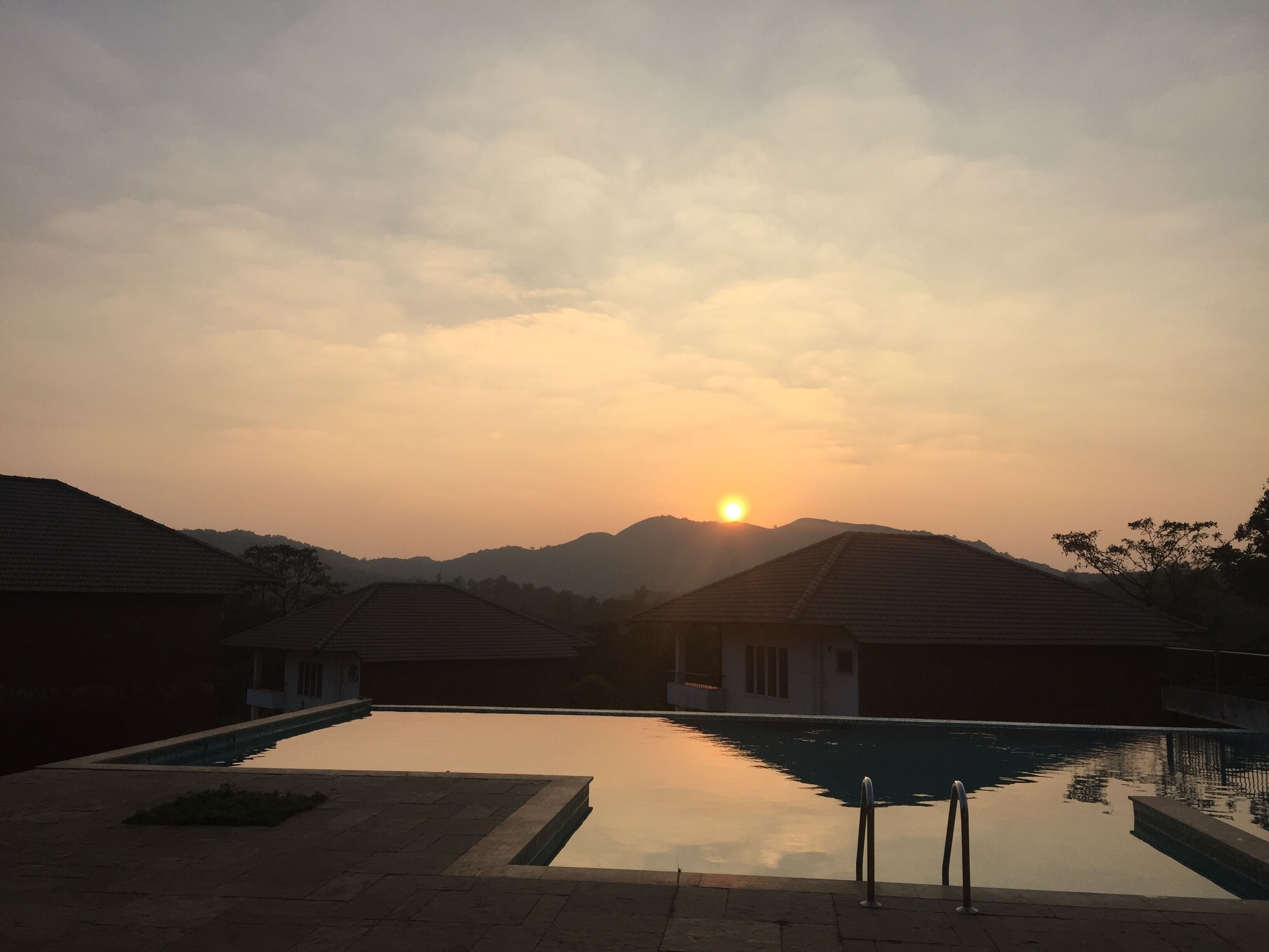 Una piscina con vista a la puesta de sol y montañas al fondo.