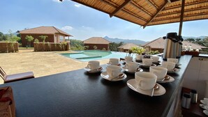 A dining area with a view of a swimming pool and mountains.