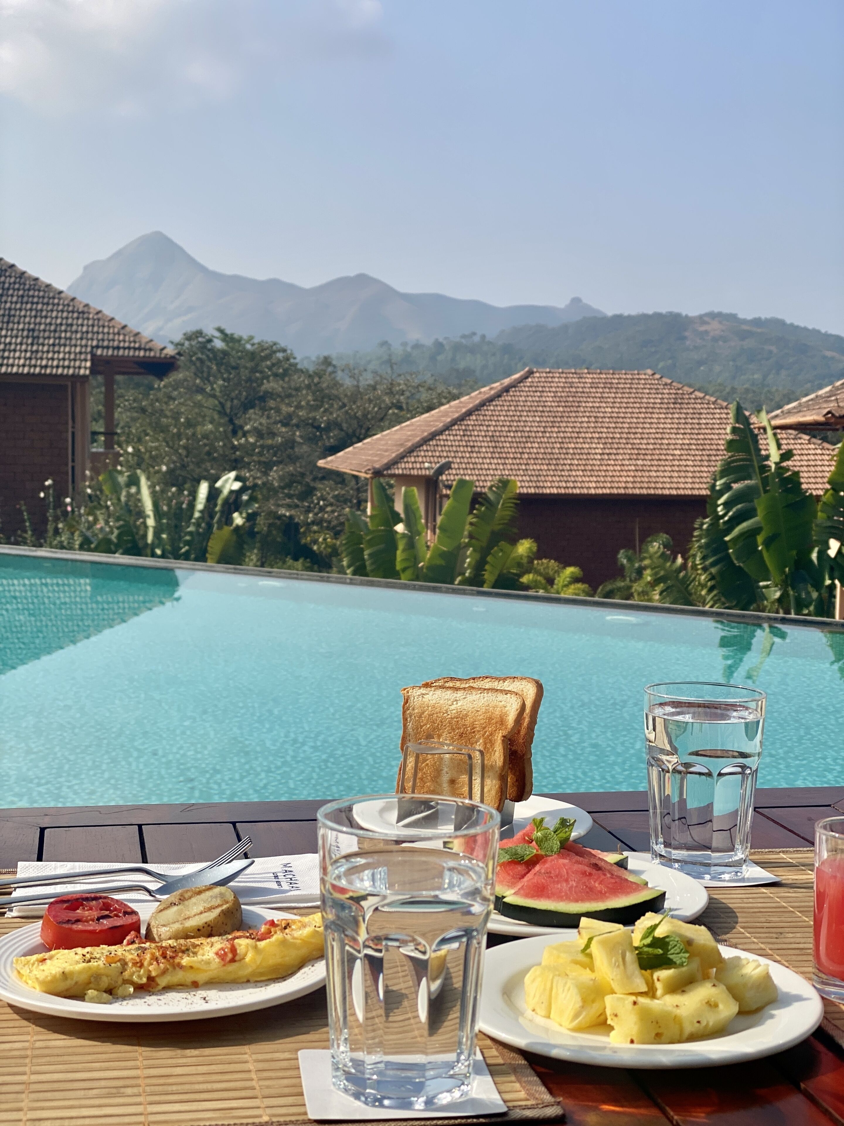 A breakfast table with toast, fruit, and a glass of water by a pool with mountains in the background.