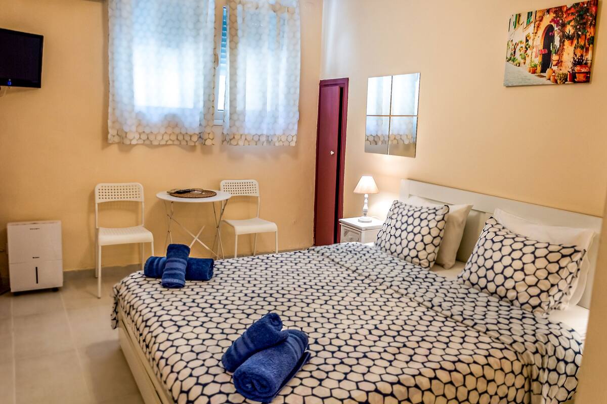 Habitación de hotel con una cama, dos sillones, una mesita, una mesita de noche, una lámpara y un cuadro en la pared.