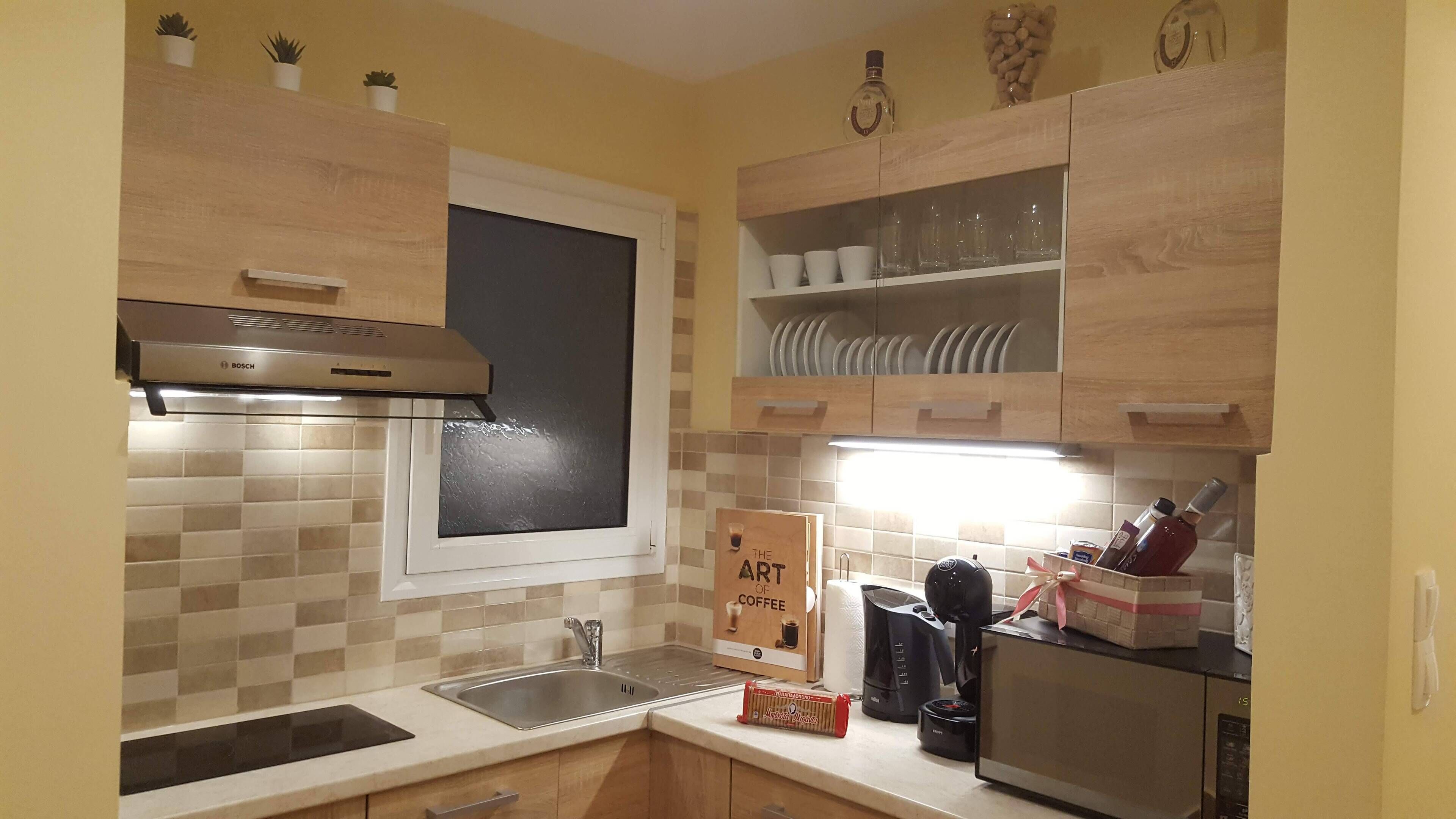 Una cocina con armarios de madera, una campana extractora Bosch, una ventana y un estante con platos y tazas.