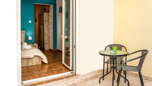 Una habitació amb un llit, una taula amb cadires i una porta corredissa de vidre que dona a una altra habitació.