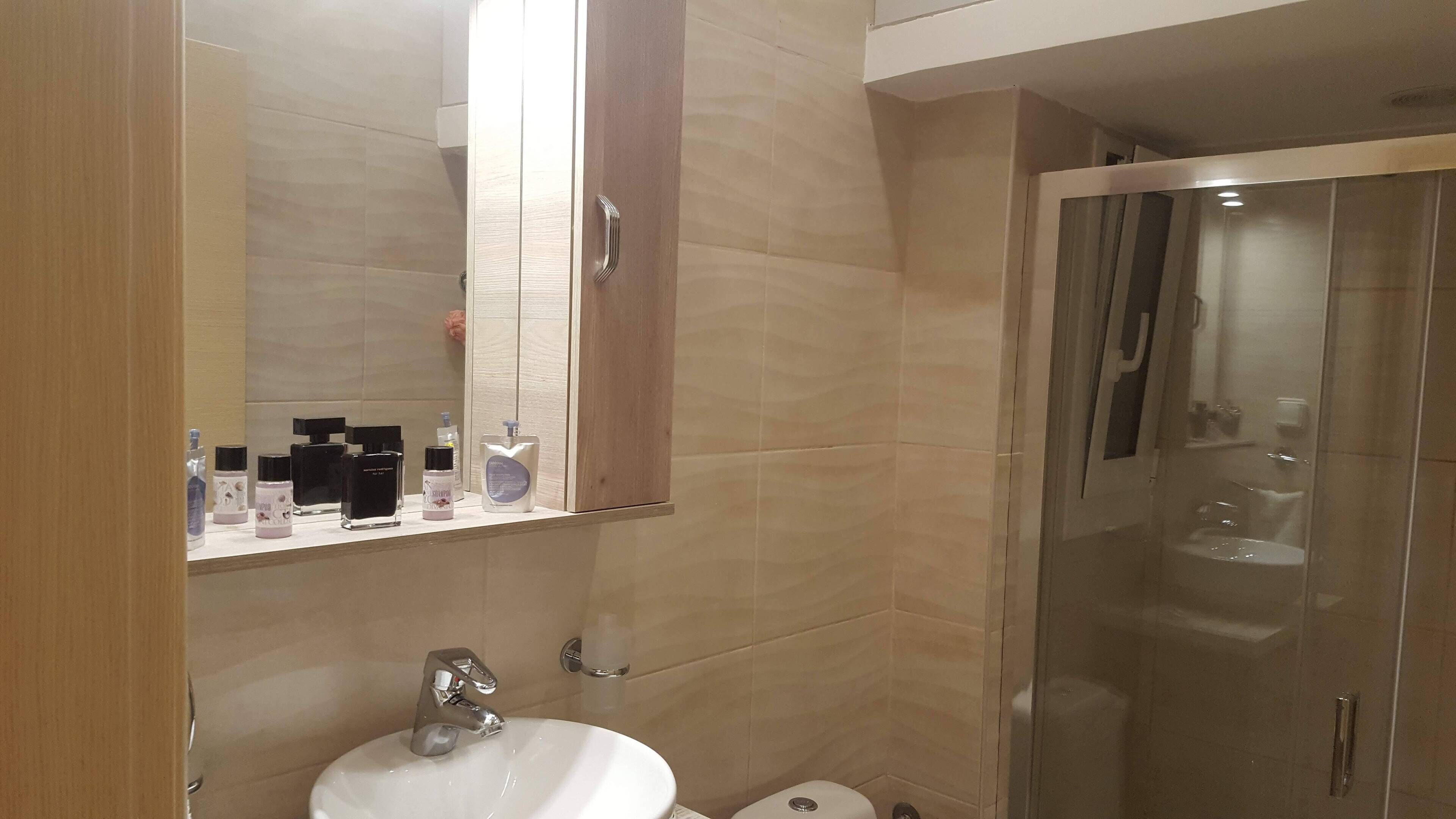 Une salle de bain moderne avec un lavabo blanc, un miroir surmonté d’une armoire en bois et une douche à parois de verre.