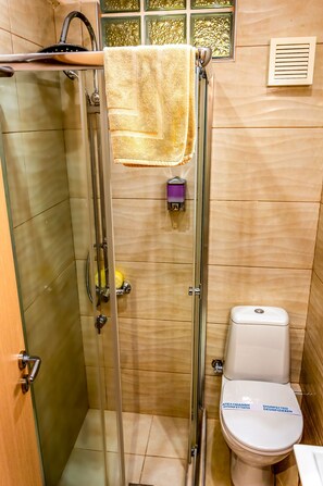 A bathroom with a glass-enclosed shower, a toilet, and a hand soap dispenser. - Zoe's Studio (Athens)