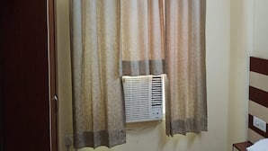 A room with a window covered by beige curtains, an air conditioning unit below the window, and a wooden wardrobe to the left. - ADB Rooms Hotel De Pal Varanasi (Varanasi)