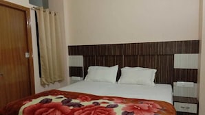 A bedroom with a bed, two pillows, a nightstand, a lamp, and a wooden door. - ADB Rooms Hotel De Pal Varanasi (Varanasi)
