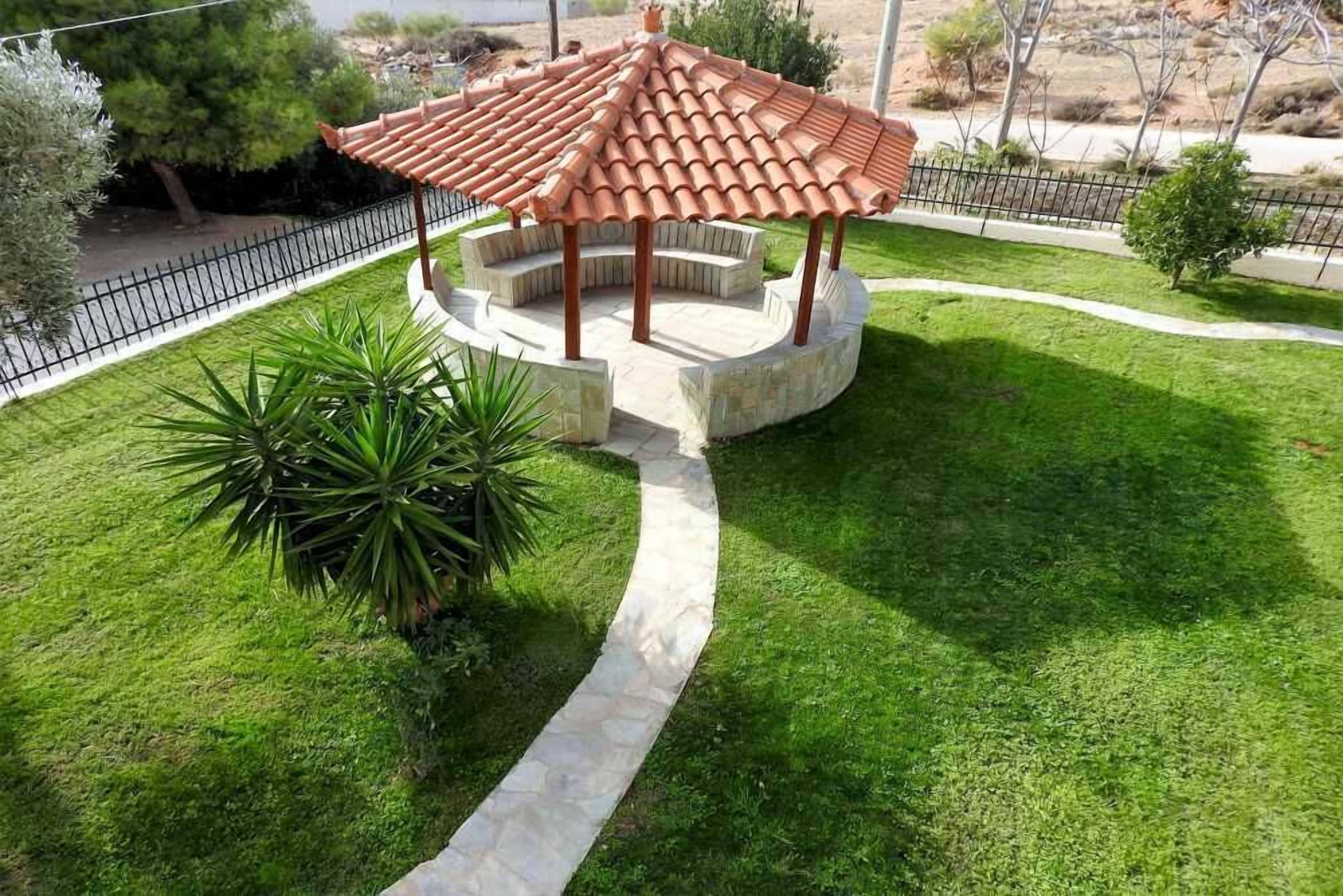 Ein Kiosk mit Ziegeldach, umgeben von einem Steinweg und üppigem Grün.