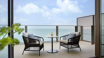 A balcony with two wicker chairs, a round table with two glasses and a bottle, and a view of the sea.