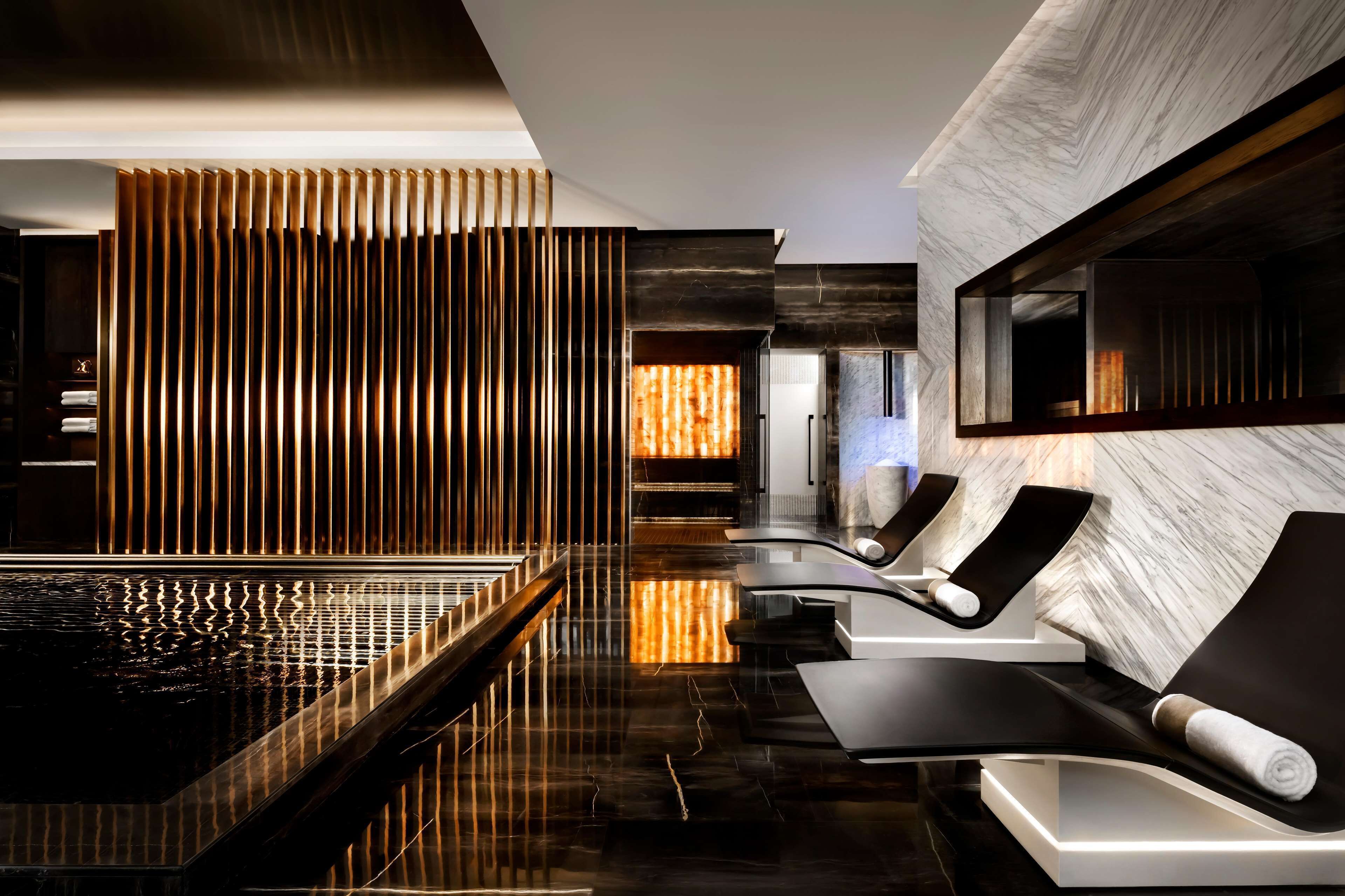 A modern spa area with a reflective pool, lounge chairs, and a wooden slat wall.