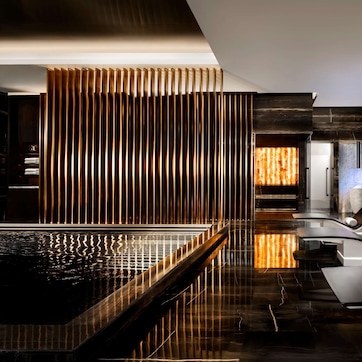 A modern spa area with a reflective pool, lounge chairs, and a wooden slat wall.