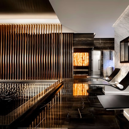 A modern spa area with a reflective pool, lounge chairs, and a wooden slat wall.